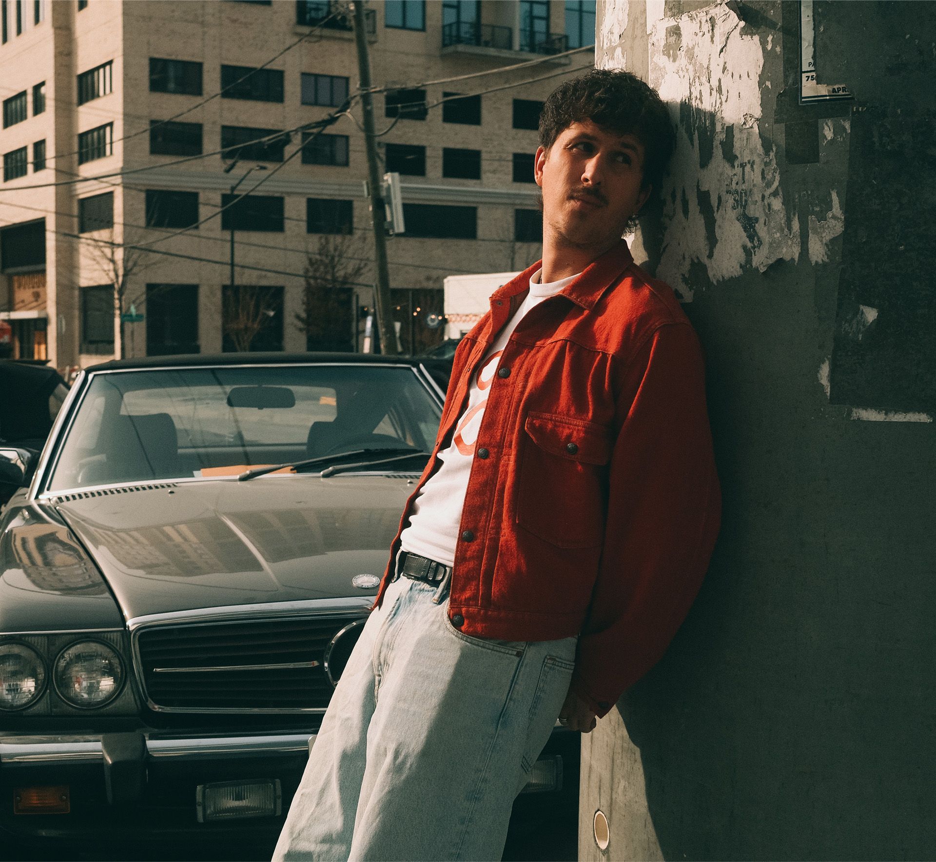 Arthur Hill leaning against a wall with a black mercedes behind him
